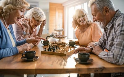 Group of happy seniors playing chess and having fun together at home.